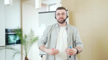 Günlük giysiler içindeki genç kendine güvenen iş adamı beyaz tahta kullanarak online bir toplantı sunumu ya da eğitimi düzenliyor. İş adamı ya da koç kameraya bakıp açıklama yapıyor. Evde ders veriyor. Web kamerası görünümü