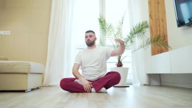 Genç sakallı yetişkin adam oturma odasında lotus pozisyonunda yerde oturmuş yoga yapıyor. Rahatlama ve meditasyon tek başına erkek nefes alma egzersizleriyle meşgul. Rahatla ve sabah dinlen.