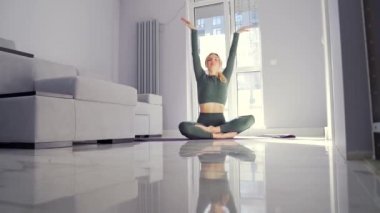 Nilüfer pozisyonunda yerde oturan ve evde tek başına yoga yapan genç bir kadının silüeti. Kadın meditasyon yapıyor ve oturma odasında dinleniyor. Huzur rahat ve sessiz bir yerde. Asana, zen