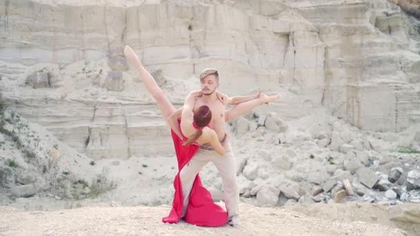 年轻热情的一对专业舞蹈家 在大自然的山顶上跳着舞 穿着红色衣服的男人和女人 背景是岩石和沙子 浪漫的现代芭蕾舞 — 图库视频影像
