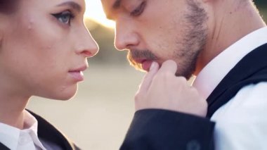 Dışarıda gün batımının arka planında birbirine bakan tutkulu bir çiftin yakın plan portresi. Takım elbiseli genç bir adam ve kadın birbirlerine sarılıyorlar. Sakallı erkek ve kızıl saçlı kadın.