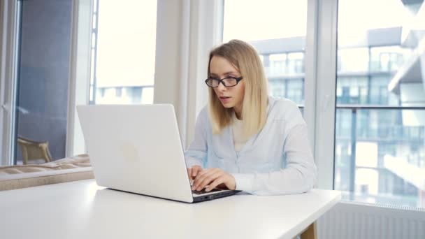 在现代写字台的笔记本电脑或电脑上工作的年轻女自由撰稿人形象 打字文字 复制或喋喋不休 女生在网上远程学习 戴眼镜的金发女 — 图库视频影像