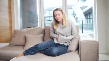 Genç bir kadın karın ağrısı şikayetiyle evdeki koltukta ya da kanepede oturuyor. Yataktaki kadın midesini regl öncesi, regl öncesi veya zehirlenme ile tutar. Sarışın kız karın ağrısından muzdarip.