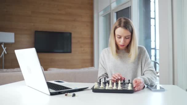形象迷人的年轻女子在线下棋游戏 在家里的厨房里桌子边使用笔记本电脑 妇女在检疫休闲和业余时间在网上游戏 — 图库视频影像