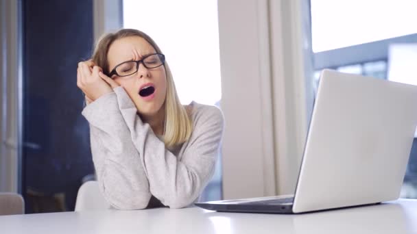 眼鏡をかけた若いブロンドの女性がノートパソコンとオーバーロードのストレッチで働いてる オフィスや自宅のコンピュータで女の子の学生は疲れや頭痛を持っています 女性の仕事によって排出される — ストック動画