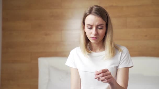 正在看快速妊娠测试的年轻女性对不想要的阴性或阳性测试感到沮丧 金发女孕妇悲伤地 失望地坐在家里 — 图库视频影像