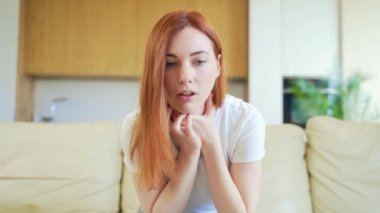 Panik atak geçiren, nefes darlığı çeken, titreyen, uyuşmuş, bilincini kaybeden genç bir kadın. Kanepede oturan bir kadının anksiyetesi ön planda. Göğüs ağrısı, korku belirtileri.