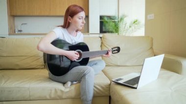Genç kızıl saçlı kız video derslerinin yardımıyla gitar çalmayı öğreniyor. Bayan kadın boş vakitlerinde kanepede dizüstü bilgisayarla oturup online müzik aleti eğitimi alıyor. Hobiler mesafesi