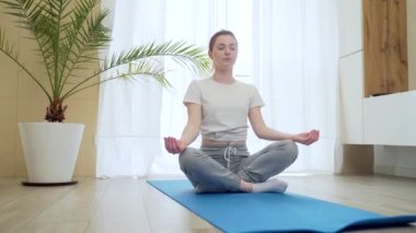Lotus pozisyonundaki genç kızıl saçlı kız evde tek başına yoga yapıyor. Gündelik giysiler içindeki aktif kadın dinleniyor ve oturma odasında mindere oturmuş meditasyon yapıyor. Kapalı alanda. Formda Kadın ve Sabah Barışı ve Sessizlik