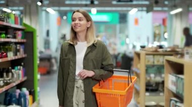 Genç beyaz kadın elinde sepetle süpermarket sıraları arasında yürüyor. Malların içinden Kadın Alışverişi Bölümü, Bakınıyor. Bir sürü koridoru olan büyük bir mağaza. Bakkalda incelenecek malları seçer.