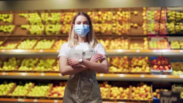 保護された顔マスク腕の中に立っている野菜セクションのスーパーマーケットで肖像若い女性労働者の売り手が交差した 果物屋市場でカメラを見ている八百屋の女性従業員作業エプロンの従業員 — ストック動画