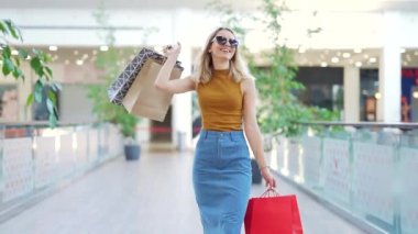 Genç mutlu sarışın çekici kadın büyük modern alışveriş merkezlerinde vakit geçiriyor. Markette yürürken renkli alışveriş torbaları taşıyan neşeli bir bayan. Alışverişten sonra tatmin olan bir kadın. İç mekan