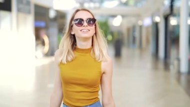 Genç mutlu sarışın çekici kadın büyük modern alışveriş merkezlerinde vakit geçiriyor. Markette yürürken renkli alışveriş torbaları taşıyan neşeli bir bayan. Alışverişten sonra tatmin olan bir kadın. İç mekan