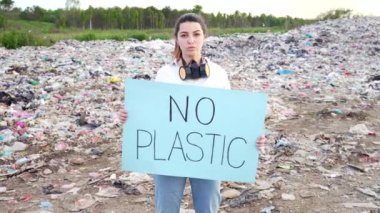 Plastiksiz poster tutan ekoloji aktivisti. Kadın ya da kız büyük bir çöp sahasının yanında duruyor. Gezegeni kirletmeyi, çevreyi kirletmeyi protesto eden kameraya bakan kız öğrenci Dünya 'yı kurtarıyor.