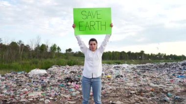 Elinde bir posterle genç bir kadın eylemcinin portresi bir çöplüğün ortasında duruyor ve doğa manzarası kız öğrencileri çevre kirliliği doğa koruma gezegenini protesto ediyor.