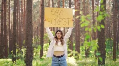 Genç kadın gönüllü eylemci, ormanı kurtaran bir posterle protesto ediyor. Elinde pankart olan kız öğrenci orman tahribatına karşı gösteri yapıyor. Koruma, koruma ortamı