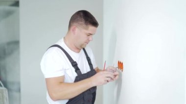 Erkek işçi, uzman elektrikçi, tamirden sonra elektrik prizi kuruyor. Adam inşaat alanındaki yeni House binasının elektrik prizi kutusunu bağlıyor.