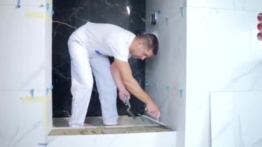 Erkek işçi, banyodaki spatulada seramik fayans yapıştırıyor. Tamir et. Tamirci havan topunu yapıştırıcı ile yapıştırıyor. Hizalanıyor, fayanslar yerleştirmeye hazırlanıyor. bitirme işi