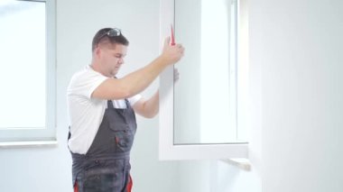 İşçi eve yeni bir plastik pencere takar ve ayarlar. Tamir, evdeki plastik pencereleri yerleştirmek ya da ayarlamak için işçi tulumunu giymeyi ve ayarlamayı düzenler. bakım hizmeti