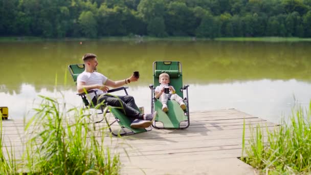 Pai Feliz Com Pequeno Filho Descansando Junto Lago Sentado Cadeiras — Vídeo de Stock