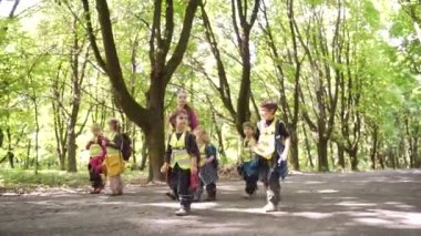 Bir grup küçük çocuk sokak arasında çocuk parkı yürüyüşü yapıyor. Çocuklar yaz kampında yürürler. Sırt çantalı anaokulu macera gezisi ormanlarında. Açık havada ahşap okulu. Seyahat tatili