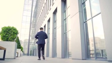 Asyalı işadamının arkadan görünüşü şehir merkezindeki modern ofis çalışmalarında hızla yükseliyor. - Dışarıda. Resmi takım elbiseli bir iş adamı arkada yürüyor.