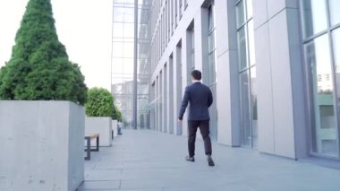 Asyalı işadamının arkadan görünüşü şehir merkezindeki modern ofis çalışmalarında hızla yükseliyor. - Dışarıda. Resmi takım elbiseli bir iş adamı arkada yürüyor.