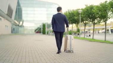 Arkadan bakıldığında Asyalı turist işadamı, resmi takım elbise giymiş kentsel arka plan şehir sokak adamı bavuluyla toplu taşıma binasında yürüyor. Modern havaalanı terminalinde bavulu çeken bir iş adamı.