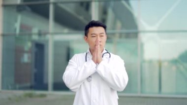 Stresli bir Asyalı doktorun portresi bir hastanenin önünde ya da dışında duruyor. Kliniğin yakınında düşünceli bir doktor. Salgın sırasında steteskoplu sağlık görevlisinin stresi.