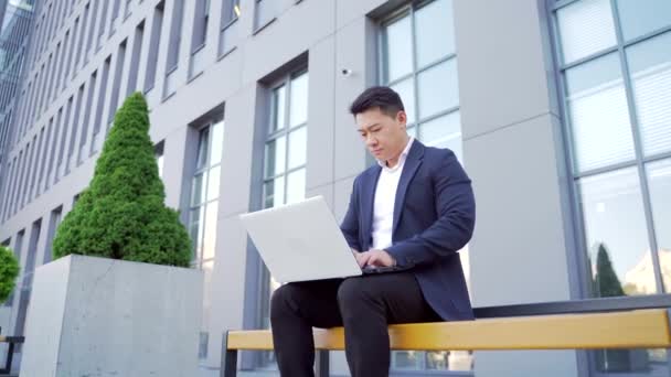 Male Asian Businessman Working Laptop Online Outdoors Sitting Bench Downtown — Stock Video