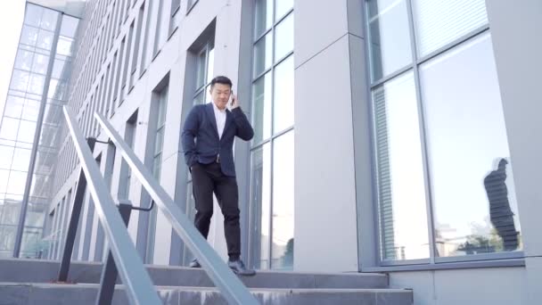 자신감 사업가가 핸드폰을 사무실 건물로 이사하는 아시아의 비지니스 이걷고 양복을 — 비디오