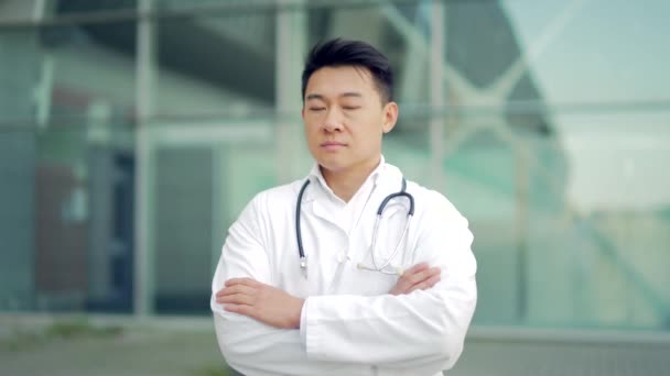 在外面的现代化医院的背景下 亚洲医生手挽手看着相机的近照 有信心的医生在室外 在诊所附近穿着洗涤剂的男性科学家治疗师 — 图库视频影像