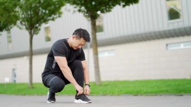 Asyalı erkek sporcu koşuya hazırlanıyor kravatlarını bağlıyor spor ayakkabılarını bağlıyor ve spor bileklik takan akıllı saat hazır. Şehir parkındaki sokak. Koşmadan önce bağcıklarını bağlıyor.