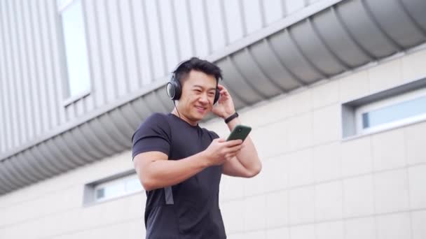 Молодий Веселий Активний Азіатський Хлопець Спортивної Ходьби Навушниками Мобільний Телефон — стокове відео