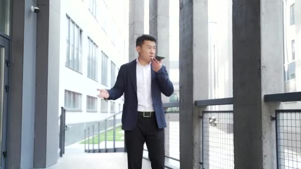 アジア系男性のビジネスマンは屋外で電話を持ってるビジネスマンの外の電話で怒ってる 緊張した狂牛病の専門家の会話スマートフォン 都市部の路上での刺激的な会話や歩行 — ストック動画