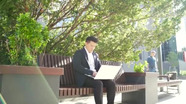 Молодой Азиатский Бизнесмен Фрилансер Сидящий Скамейке Работающий Ноутбуком Городском Парке — стоковое видео