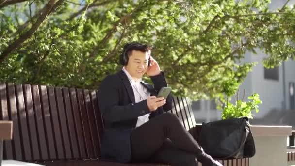 Cheerful Asian Business Man Sitting Bench City Park Downtown Listening — Stock Video