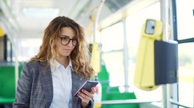 Şehir içi taşımacılığa cep telefonu uygulaması ile ödeme yapan bir kadın. Modern kadın yolcu otobüs biletini onaylamak için akılsız akıllı telefon kullanıyor. Beyaz tenli öğrenci troleybüs ya da tramvay kullanım uygulaması içinde