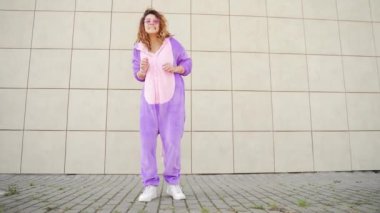 Sarı duvarda dans eden neşeli, mutlu, genç bir kadın. Tek boynuzlu at kostümlü maskeli çılgın kız. Eğlence insanları, mutluluk, neşe Şehir sokaklarında modern yaşam tarzı