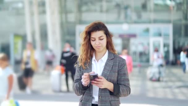 通行人の群衆の間に都市の通りの背景に立って若い魅力的なビジネス女性 そして外の携帯電話を使用して スマートフォンを手にしたサラリーマン — ストック動画