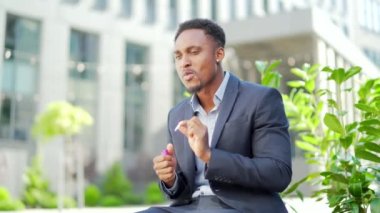 Afro-Amerikan iş adamı kenevir içiyor şehir parkındaki bankta oturuyor. Erkek işçi, iş adamı. Takım elbiseli bir ofis çalışanı dışarıda bir marihuanayı rahatlatıyor.