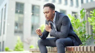 Afro-Amerikan iş adamı kenevir içiyor şehir parkındaki bankta oturuyor. Erkek işçi, iş adamı. Takım elbiseli bir ofis çalışanı dışarıda bir marihuanayı rahatlatıyor.