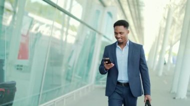 Başarılı genç, kendinden emin Afro-Amerikan iş adamı cep telefonuyla modern ofis arka planına karşı hareket ediyor. Siyah iş adamı resmi takım elbise içinde cep telefonuyla yürüyor.