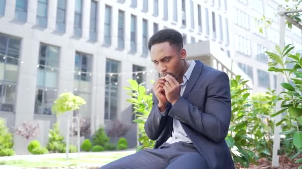 アフリカ系アメリカ人のビジネスマンが屋外で大麻を吸ってる街の公園のベンチに座ってる 男性社員ビジネスマン スーツのオフィスワーカーは外のマリファナのストレスを緩和する — ストック動画