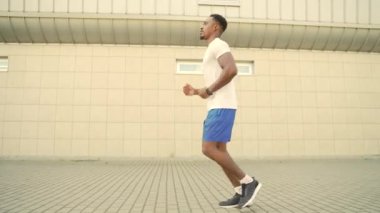 Genç Afro-Amerikan erkek atlet modern sarı duvar kentsel arka planında koşuyor. Sabah koşusu siyahi bakış açısı. Şehir caddesinde aktif sağlıklı yaşam tarzı