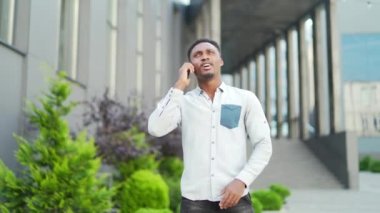 Neşeli Afro-Amerikalı adam şehir sokaklarında günlük kıyafetlerle dolaşır ve konuşur. Akıllı telefonlu hippi bir erkek modern arka plana ters düşer. Mutlu, gülümseyen siyah adam sohbeti.