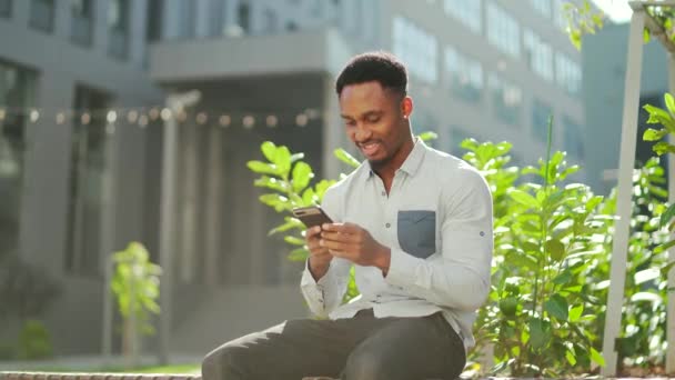 Веселый Африканский Американец Пользующийся Мобильным Телефоном Сидит Скамейке Городском Парке — стоковое видео
