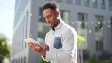 Afro-Amerikan adam tablet kullanıyor. Şehir sokaklarında kentin arka planında bankta oturuyor. Zenci adam elinde bir alet ya da akıllı telefon tutarak okuyor ya da alışveriş yapıyor. Kampüste bir öğrenci. Dışarıdaki serbest çalışan.