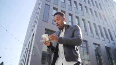 Mutlu, başarılı Afrikalı Amerikalı adam sayıyor, el sallıyor, atıyor, gösteriş yapıyor, para kazanıyor, şehir binası. Kameraya bakan adam borsada kazananı kutluyor.