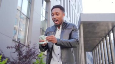 Mutlu, başarılı Afrikalı Amerikalı adam sayıyor, el sallıyor, atıyor, gösteriş yapıyor, para kazanıyor, şehir binası. Kameraya bakan adam borsada kazananı kutluyor.